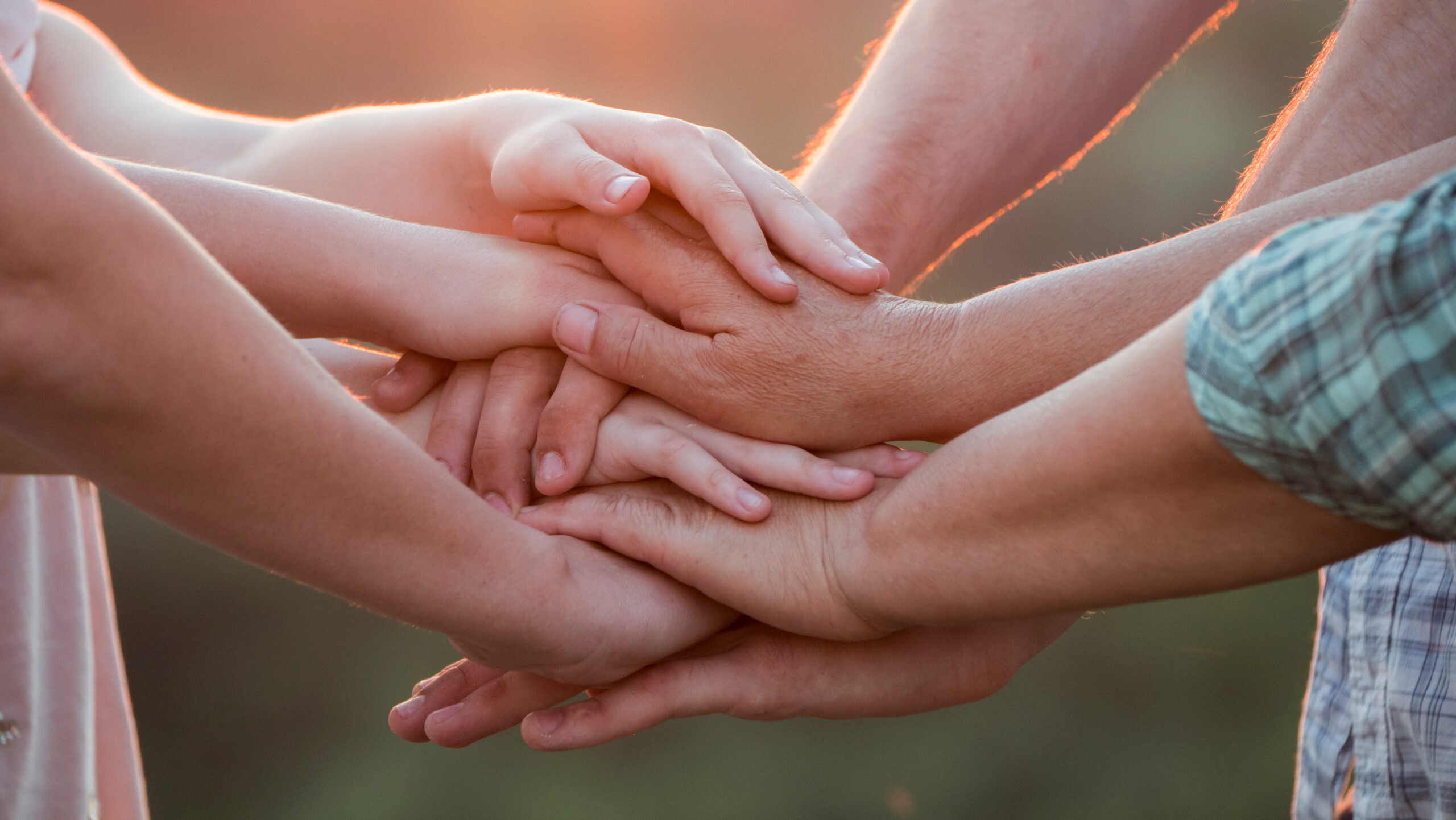 Mehrere Hände verschiedener Menschen liegen übereinander und symbolisieren Teamarbeit, Zusammenhalt und Gemeinschaft.