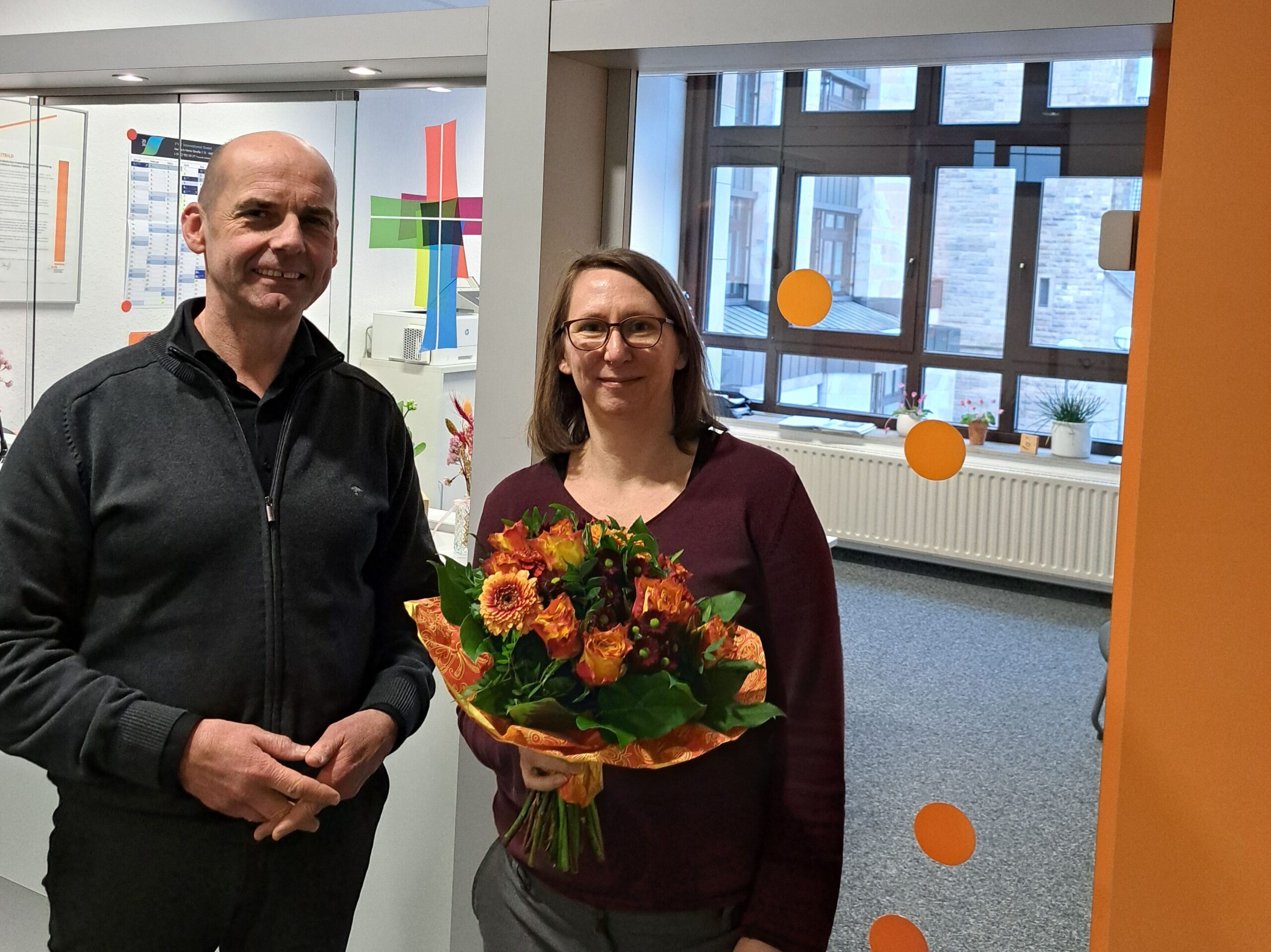 Links Herr Sasse, rechts Frau Schmitten mit einem Blumenstrauß