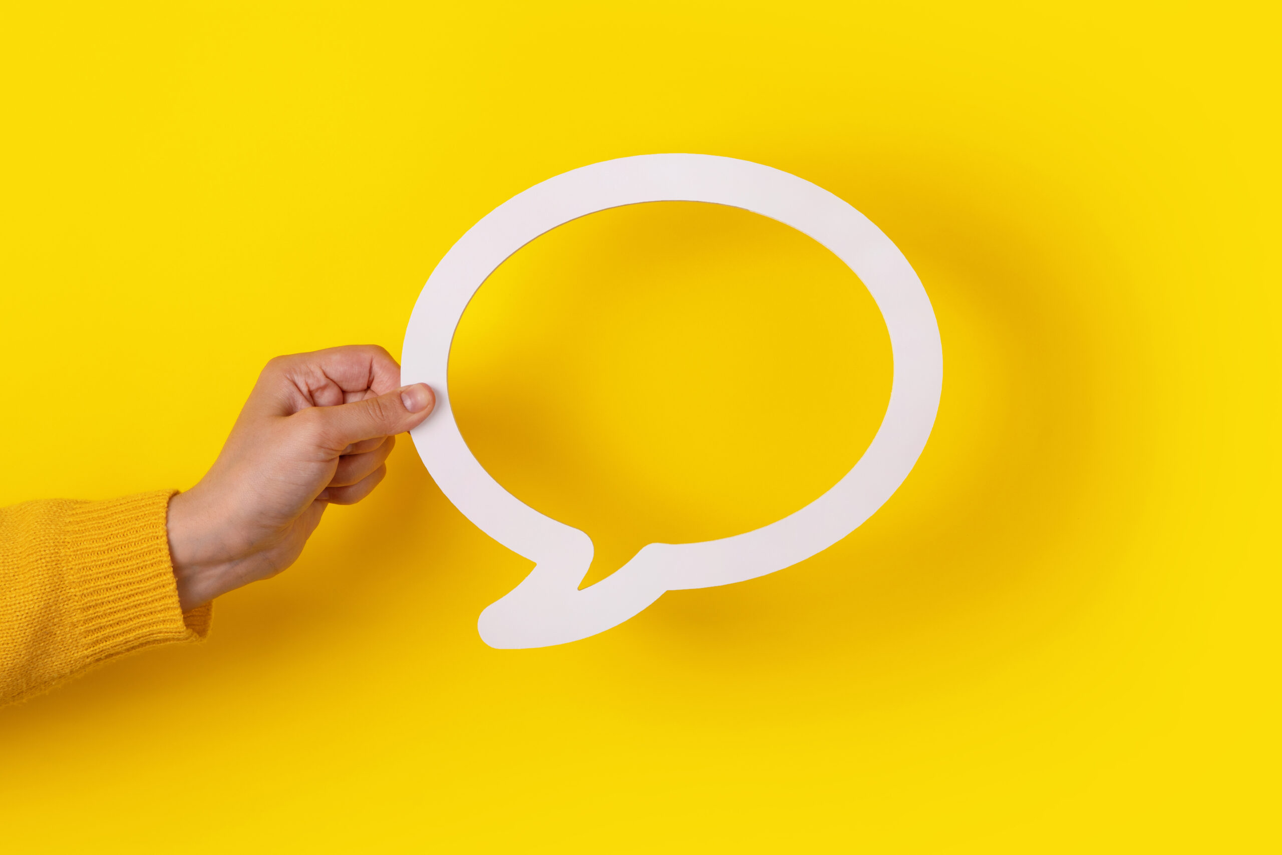 Hand hält eine leere Sprechblase vor gelbem Hintergrund – Symbol für Dialog, Austausch, Beteiligung und offene Kommunikation.